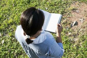 menina lendo uma livro dentro a frente Jardim fêmea aluna retrato, Educação conceito feliz fofa criança sorridente com aprendizado. foto