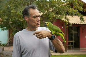 homem lado de fora segurando e jogando com dele azul frontal Amazonas papagaio foto