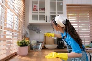 ásia jovem mulher limpeza janela dentro a cozinha. tarefas domésticas conceito foto