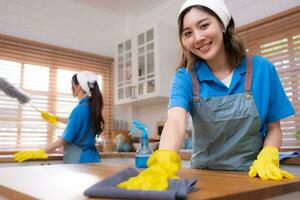 retrato do jovem ásia mulher limpeza a mesa dentro a cozinha às casa foto