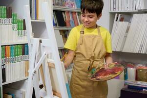 hispânico primário escola estudante, adolescente Garoto tendo Aulas às arte estúdio, Aprendendo desenho, pintura em pé às cavalete foto