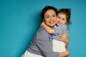 alegre mãe abraçando dela filha. azul fundo, feliz mãe dia conceito, crianças proteção dia foto