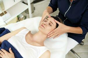 esteticista fazendo facial anti-envelhecimento elevação massagem em mulher face às spa clínica. profissional linfático drenagem massagem às spa Centro foto