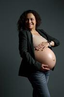 atraente latim americano grávida mulher segurando barriga dentro a semana 36 do despreocupado gravidez, olhando a parte, de lado uma cópia de espaço foto