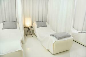lindo luxuoso branco interior do uma massagem quarto com dois camas para dois pessoas para relaxar e dentro uma moderno bem estar spa foto