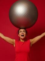 retrato do uma ginástica feliz africano americano em forma mulher em pé segurando uma em forma bola dentro dela elevado braços acima dela cabeça. cópia de livre espaço para texto. foto