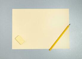 plano deitar foto do amarelo apagador, lápis e Folha do papel em uma cinzento superfície