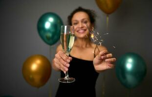 suave foco em flauta do champanhe ou espumante vinho e estrelinhas dentro a mãos do feliz mulher tendo Diversão às aniversário, aniversário festa, Natal Novo ano evento. cinzento fundo com ar dourado bolas foto