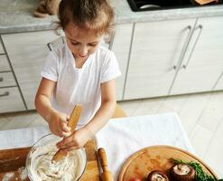 topo Visão do fofa bebê menina focado em amassar massa. pizza ingredientes em volta de madeira corte borda foto