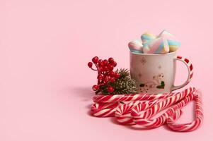 lindo minimalista Natal composição com quente chocolate beber decorado com marshmallows e listrado pirulitos, doce bengalas isolado sobre Rosa colori Backgroud com cópia de espaço para de Anúncios foto