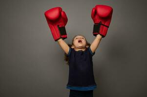 conceito do golpe para preços em cinzento fundo com cópia de espaço. pequeno criança, adorável menina boxer vestindo vermelho boxe luvas levanta mãos dentro vencedora posição. tiroteio para boxe dia e Preto Sexta-feira foto