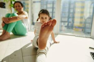 foco em pé do uma pequeno menina exercício com dela mãe às casa foto