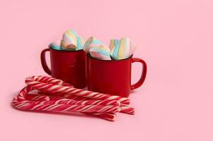 café canecas com marshmallows e doce bengalas em Rosa colori fundo. Natal quente beber com sobremesas. quente chocolate, copo do café cacau. Novo ano, alegre Natal feriado celebração foto