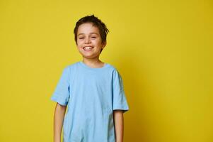 isolado retrato em amarelo fundo do uma criança Garoto rindo e expressando felicidade e brincalhão humor, posando para a Câmera. foto