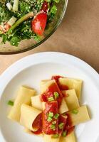 plano deitar. cortada foto do uma saudável vegano refeição consistindo do vegetariano erva salada e cozinhou italiano massa com tomate molho e verde cebola guarnição, enfeite, adorno