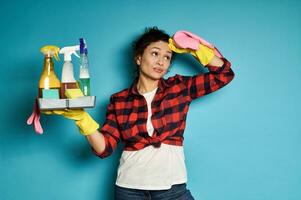 fofa dona de casa com bandeja do limpeza Ferramentas e produtos Exausta depois de trabalho de casa. azul fundo com cópia de espaço foto