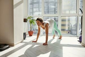 jovem mulher praticando ioga posturas às lar. ioga pose do para cima voltado para cachorro foto