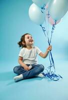 fofa sorridente pequeno menina sentado em azul fundo com suave sombra e segurando balões dentro a mão. infância e criança proteção dia conceito. cópia de espaço foto