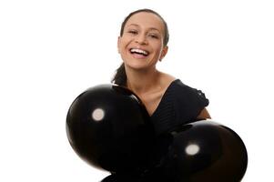 Preto Sexta-feira conceito com a atraente misturado raça bonita mulher com lindo cheio de dentes sorriso, vestido dentro Preto parece às a Câmera carrinhos com Preto ar balões contra branco fundo, cópia de espaço. foto