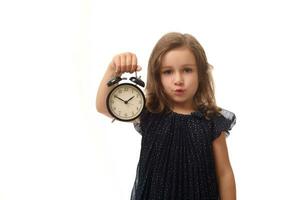 lindo bonita europeu 4 anos velho bebê menina com a alarme relógio dentro dela mão e parece às Câmera, isolado sobre branco fundo com cópia de espaço foto