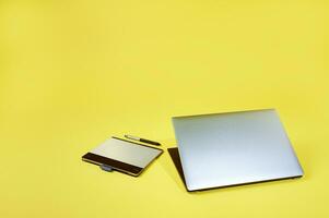 esfolar deitar composição do uma prata cinzento computador portátil deitado perto uma gráficos tábua isolado em uma amarelo fundo. cópia de espaço foto