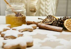 foco em querida dentro transparente vidro garrafa e seco laranja fatias, pinho galhos e cones em pergaminho papel e borrado Pão de gengibre biscoitos borrifado com açúcar pó em primeiro plano foto