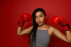 boxe chamion afro garota, atleta mulher boxer vestindo vermelho luvas, levantando dela mãos acima, olhando às Câmera, isolado sobre vermelho colori fundo com cópia de espaço. contato marcial arte e vitória conceito foto