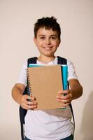 sorridente feliz escola criança segurando Fora às Câmera caderno com cópia de espaço para seu Publicidades., isolado sobre branco fundo. foto