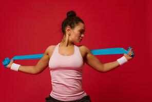 africano americano muscular mulher fazendo alongamento exercícios em braços usando elástico ginástica banda contra vermelho fundo com cópia de de Anúncios espaço foto