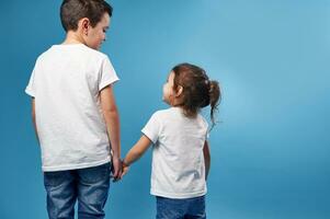 uma Garoto e uma menina ficar de pé com seus costas para a Câmera em uma azul fundo e Veja às cada de outros segurando mãos apertado. foto