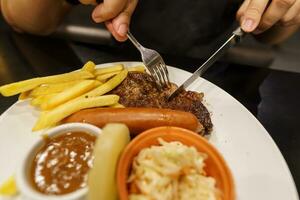 homem comendo grelhado carnes estaca a partir de placa. mão segurando faca e garfo corte grelhado carne bife foto