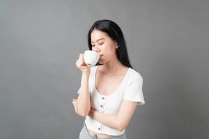 jovem mulher asiática com um rosto feliz e uma mão segurando uma xícara de café