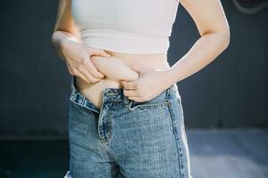 mulher gorda, barriga gorda, gordinha, mão de mulher obesa segurando gordura excessiva da barriga com fita métrica, conceito de estilo de vida de dieta de mulher foto