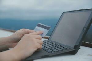 conectados pagamento, jovem mulher segurando crédito cartão e digitando em computador portátil foto