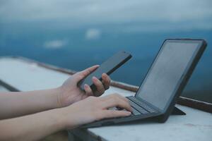 jovem o negócio mulher trabalhando às a computador dentro cafeteria em a Rocha. jovem menina redução de marcha trabalhando às uma computador portátil às pôr do sol ou nascer do sol em a topo do a montanha para a mar, trabalhando dia. foto