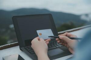 conectados pagamento, jovem mulher segurando crédito cartão e digitando em computador portátil foto