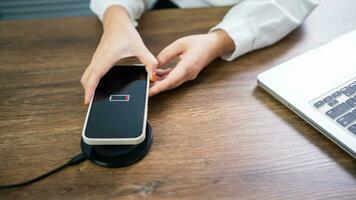 cobrando Móvel telefone bateria com sem fio cobrando dispositivo dentro a mesa. Smartphone cobrando em uma cobrando almofada. Móvel telefone perto sem fio carregador moderno estilo de vida tecnologia conceito. foto