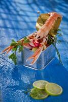 uma camarão dentro uma recipiente com uma Lima em uma azul mesa foto