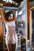 sensual menina dentro frente do a geladeira olhando para alguns fresco foto