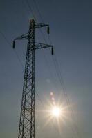 uma silhueta do a eletricidade torre com a Sol atrás isto foto