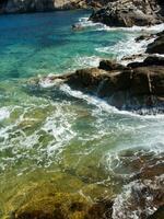 uma rochoso costa com ondas falhando contra a pedras foto