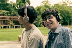 jovem ásia adulto casal vestindo fones de ouvido, sentado, ouvindo para música e gastos livre Tempo juntos dentro frente do seus casa, Boa relação e melhor amigos conceito. foto