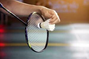 badminton jogador detém raquete e branco creme peteca dentro frente do a internet antes servindo isto para outro lado do a quadra foto