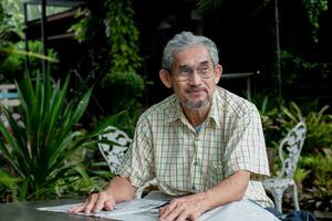 ásia idosos homem sentado e lendo jornal dentro a quintal do dele casa, suave e seletivo foco, tempo livre atividade do Senior pessoas conceito. foto