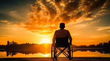 silhueta do Desativado homem em cadeira de rodas às a de praia durante pôr do sol, desabilitar dia foto