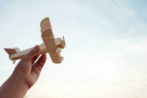liberdade conceito, humano mão segurando de madeira avião em a pôr do sol céu fundo foto