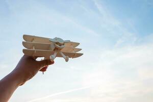 liberdade conceito, humano mão segurando de madeira avião em a pôr do sol céu fundo foto