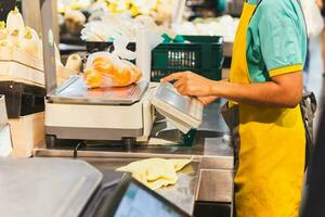 mercearia loja funcionários pesagem laranjas dentro plástico saco em digital escalas. foto