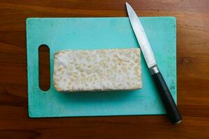 fresco cru tempeh, em uma corte borda e faca para cortando. Comida preparação conceito foto