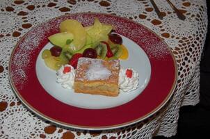 servido saboroso sobremesa em uma ampla prato em uma reto branco toalha de mesa com fruta foto